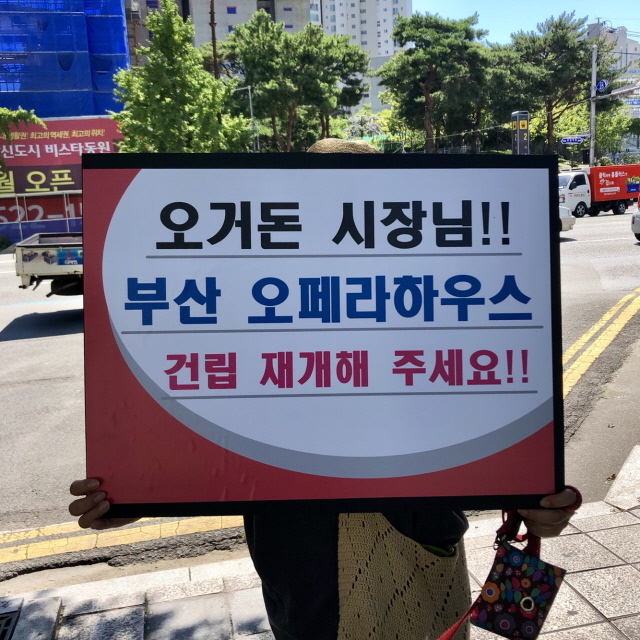 ▲ 5일 부산시청 시민광장 앞에서 '부산오페라하우스 건립 촉구 범시민궐기대회'에 참여한 시민이 오페라하우스 건립 재개 피켓을 들고 있다. ⓒ프레시안