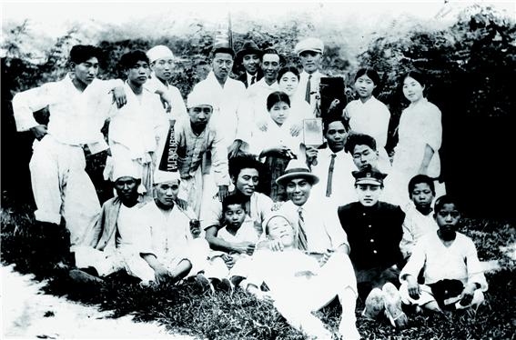 ▲영화 아리랑의 출연진과 스테프들. 1926년. 맨 앞줄 소년을 안고있는 사람이 최영진 역의 나운규, 오른쪽 옆 중절모차림이 일제에 아부하는 오기호 역의 주인규, 그 옆 학생복 차림이 영희를 사랑하는 윤현구 역의 남궁운(김태진), 촬영기 바로 왼쪽의 소녀가 '한국 농촌의 정령' 여주인공 영희 역의 신일선이다. 사진 속 두 인물은 조선키네마 로고가 박힌 메가폰을 머리에 얹고 있다. 영화촬영은 고대 앞 안암골 한적한 산골동네에서 했다. C 홍기영자료사진, 눈빛출판사제공